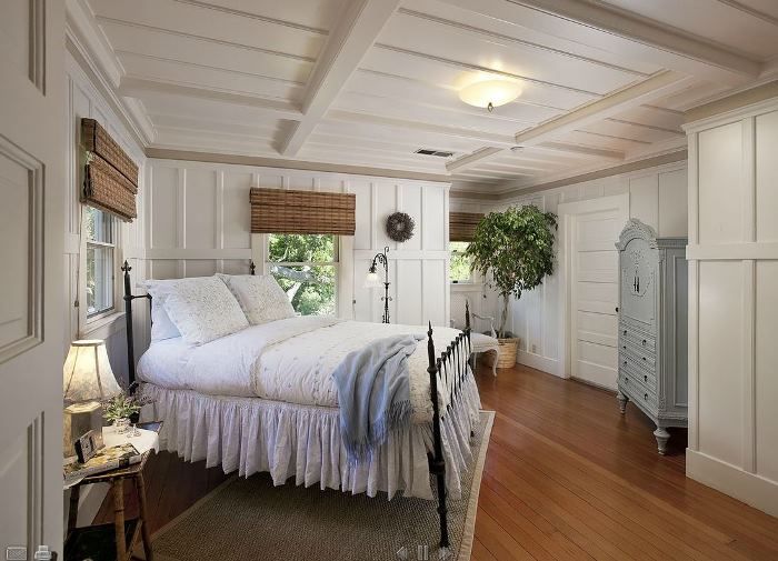 a bedroom with white walls and wood flooring has a large bed in the corner