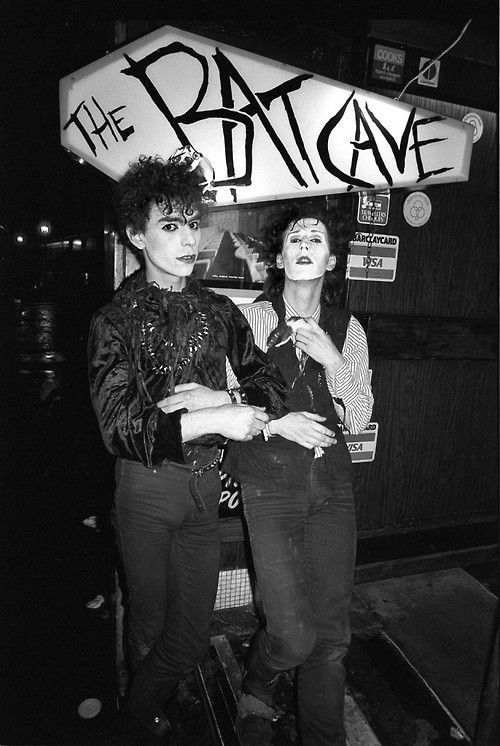 two women standing next to each other in front of a sign that says the patcave