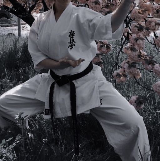 a man in white is doing karate on the grass and trees with pink flowers behind him