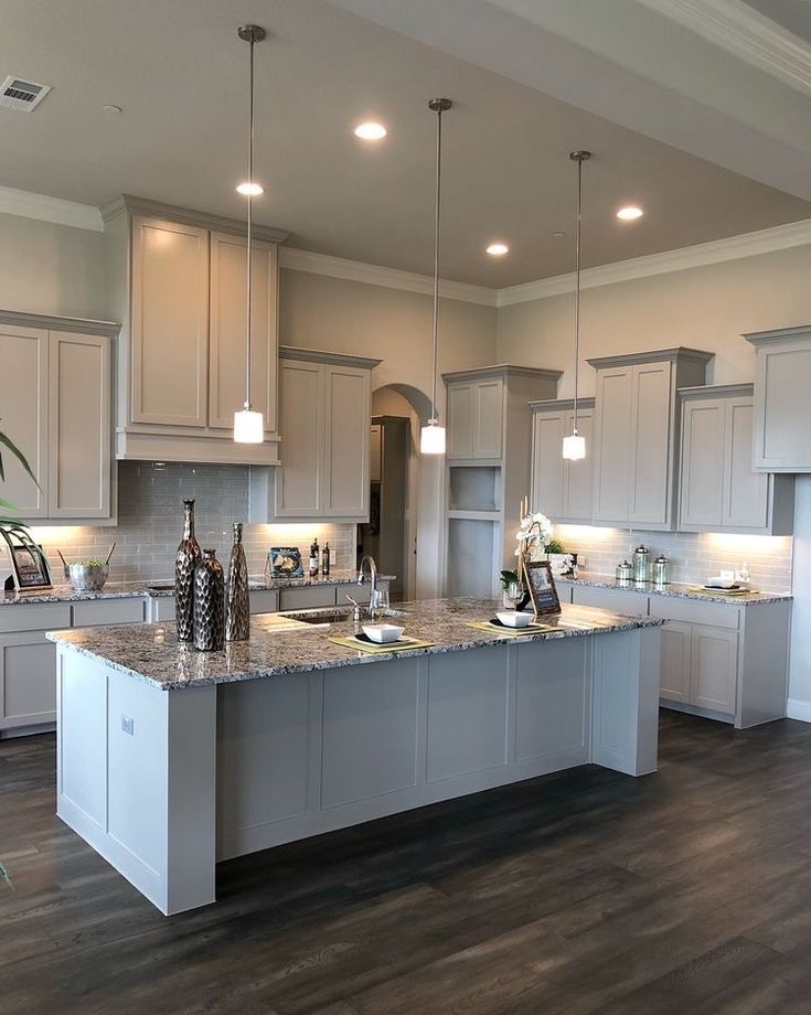 a large kitchen with white cabinets and gray counter tops, lights above the island in front of the sink