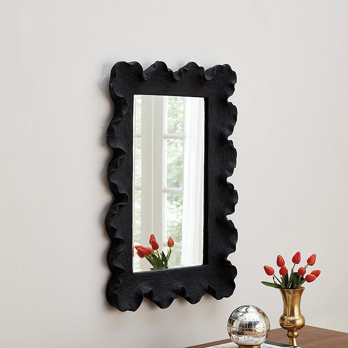 a mirror sitting on top of a wooden table next to a vase with red flowers