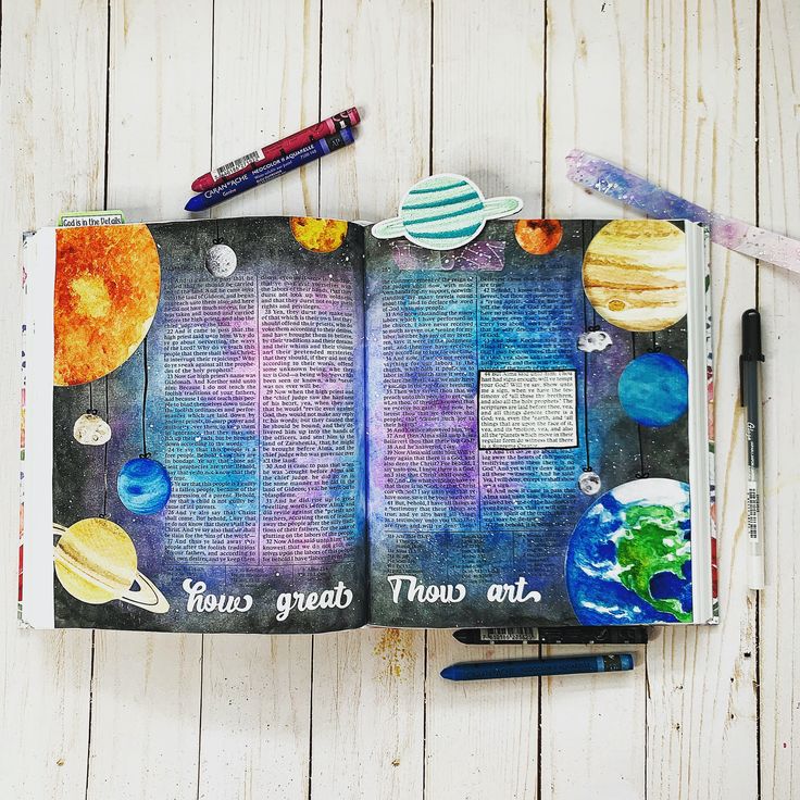 an open book with space themed pages and writing on it, surrounded by pens and markers