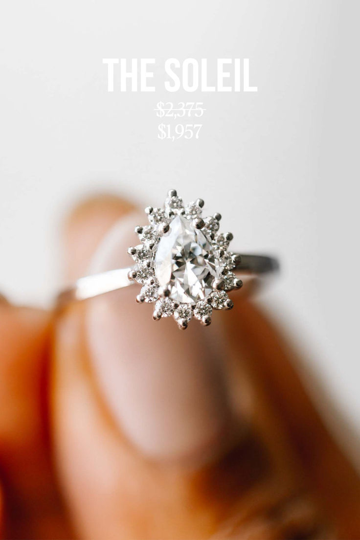 a hand holding a diamond ring with the soleil on it's finger, in front of a white background