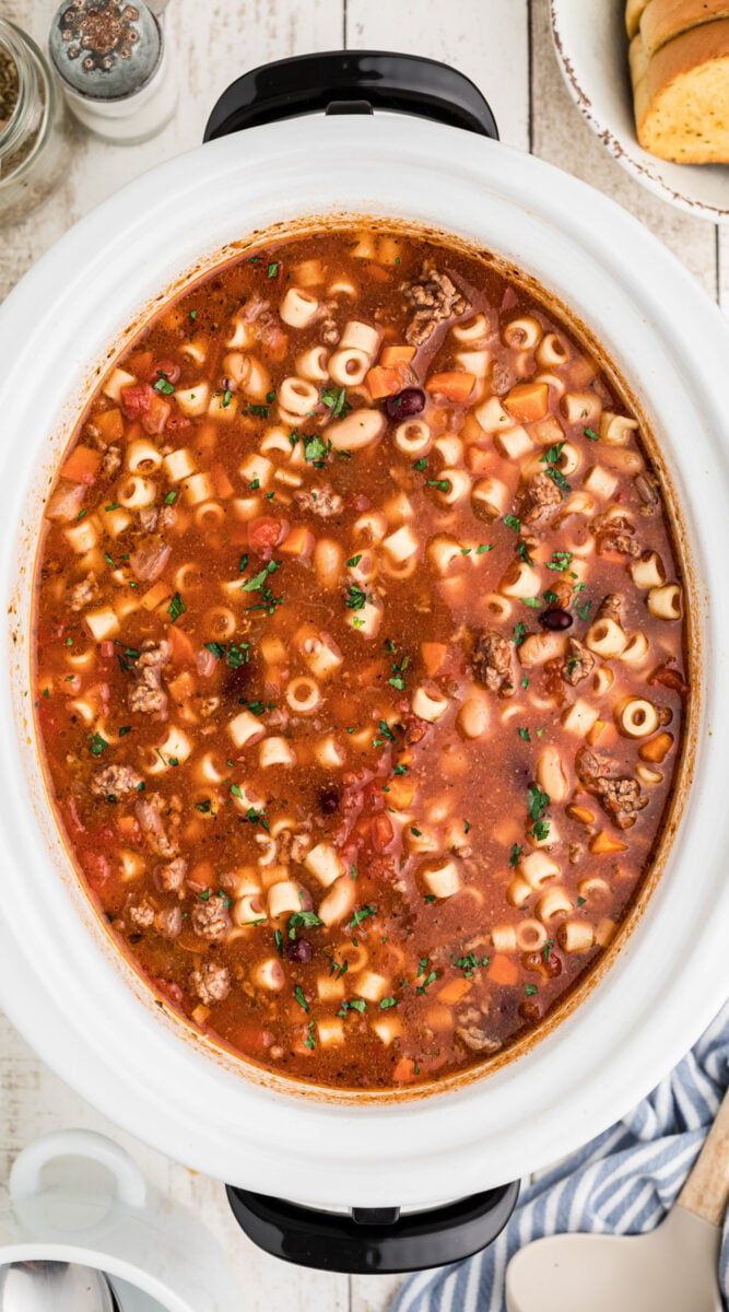 a white bowl filled with pasta and meat soup on top of a table next to bread