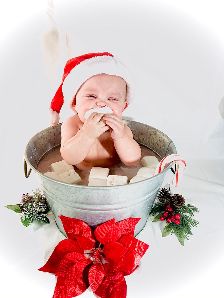 a baby in a bucket with marshmallows, candy cane and santa hat