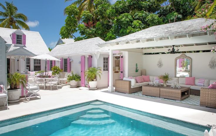 an outdoor living area with couches and tables next to a pool surrounded by palm trees