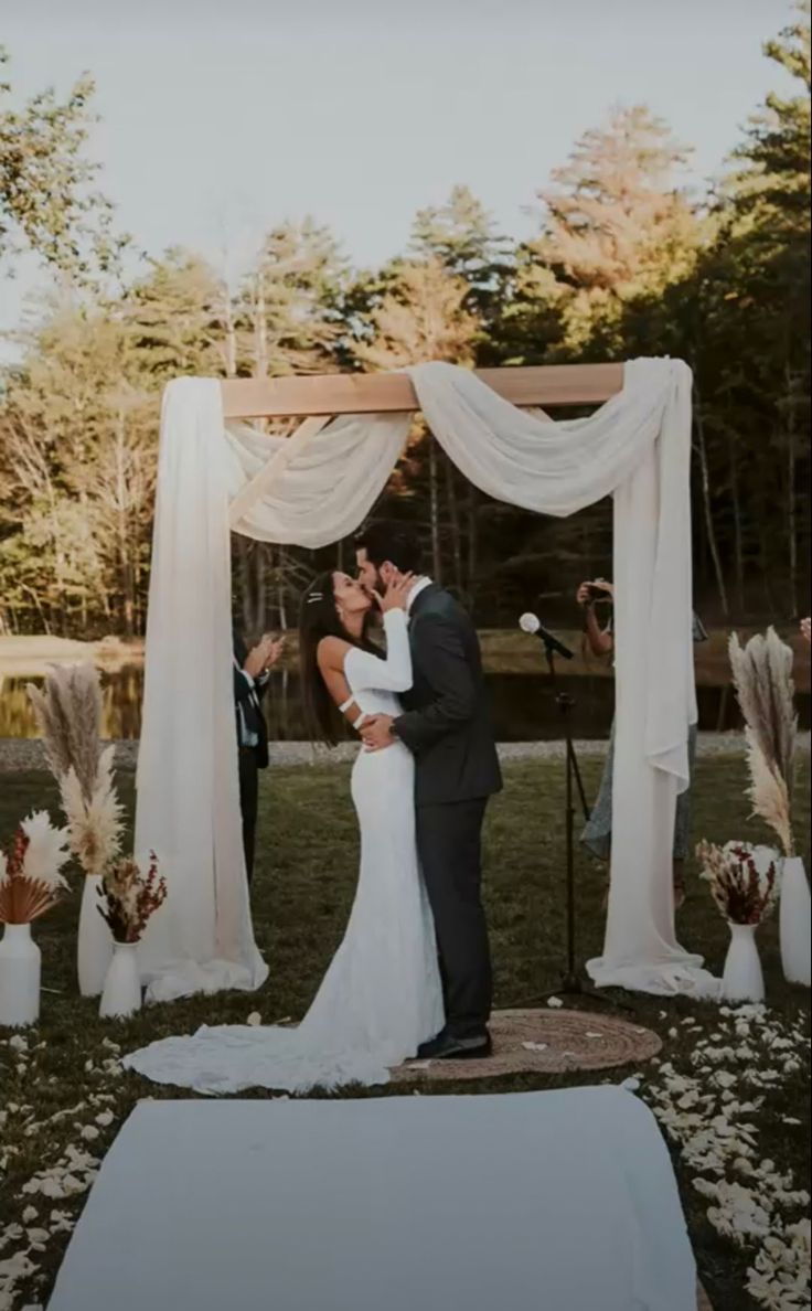 a bride and groom kissing under an outdoor wedding ceremony arch with flowers on the ground