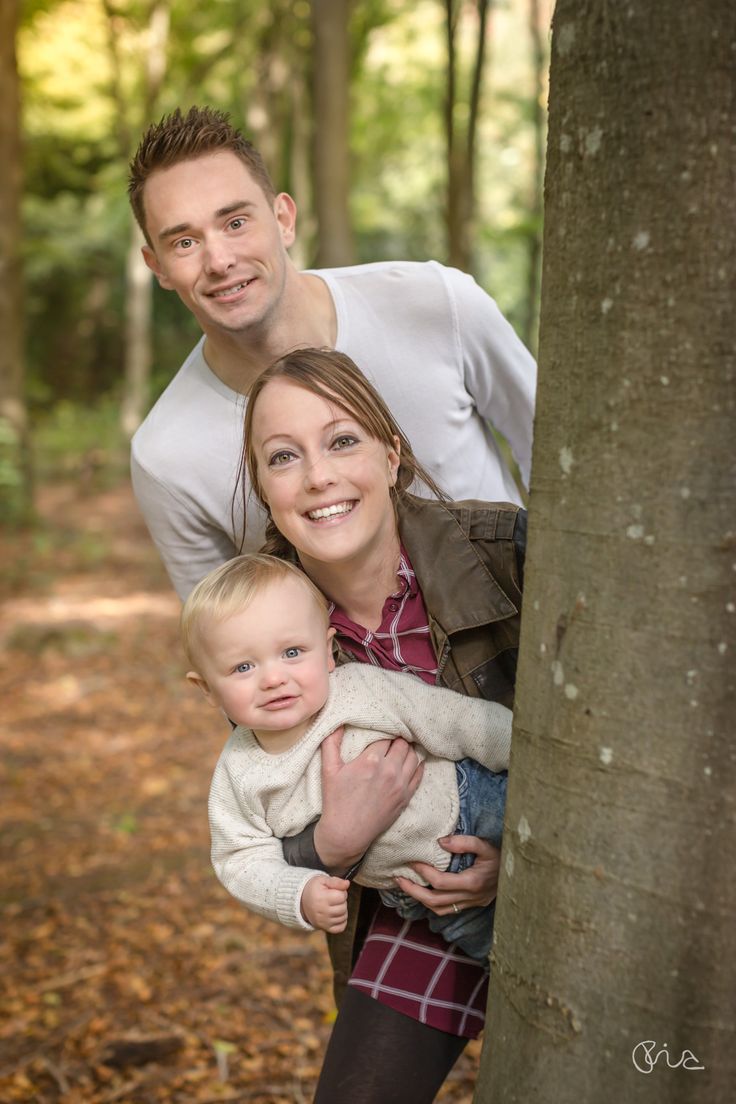 a man and woman holding a baby next to a tree