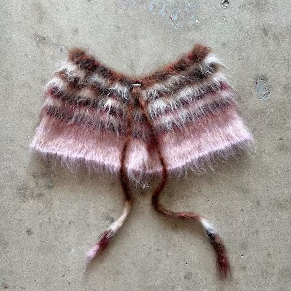 a pink and white knitted object laying on the ground