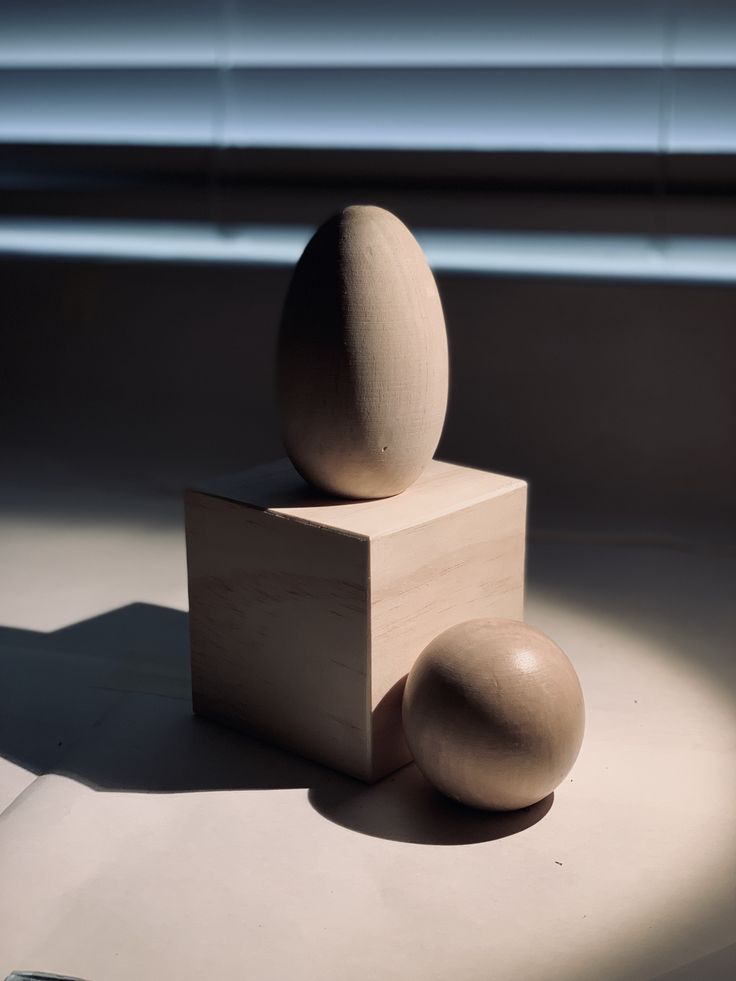 an egg sitting on top of a wooden block next to two smaller eggs in front of a window