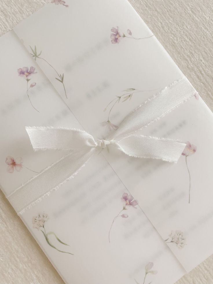 a close up of a wedding card with a bow on it's ribbon and flowers