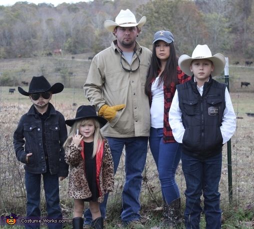 a man and two children standing next to each other in front of a cow pasture