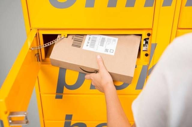 a person holding a box in front of a yellow locker with the amazon logo on it