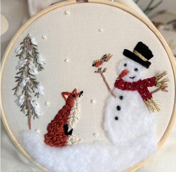 a snowman and a fox are together in this embroidery art piece, which is hanging on the wall