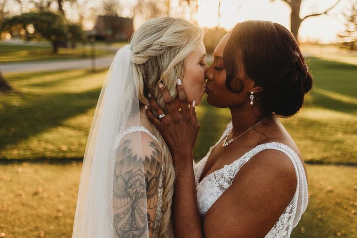 two women are kissing each other in front of the camera on their wedding day at sunset