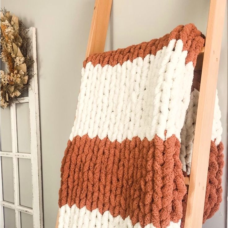 an orange and white crocheted blanket hanging on a ladder