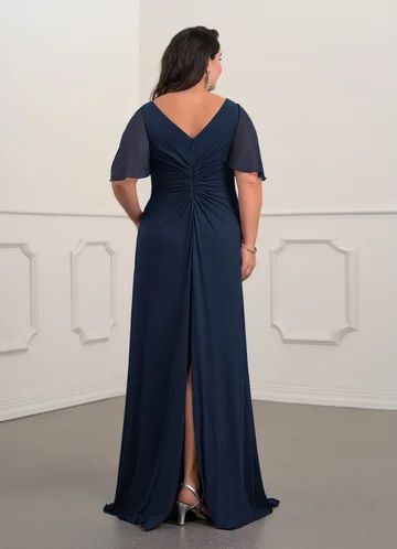 a woman standing in front of a white wall wearing a dress with a slit down the side