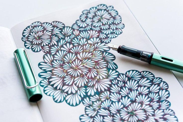 a pen sitting on top of an open notebook next to a flower design drawn in ink