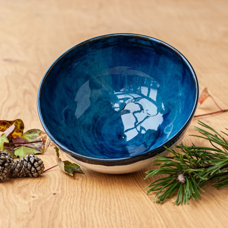 a blue bowl sitting on top of a wooden table next to pine cones and leaves