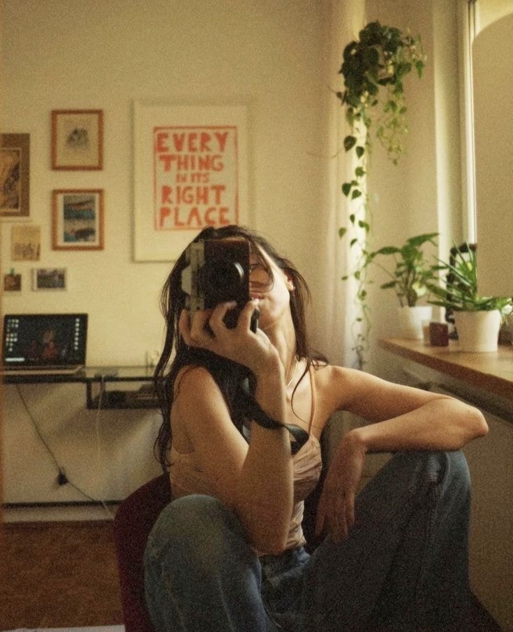 a woman sitting on the floor talking on her cell phone while holding a camera up to her face