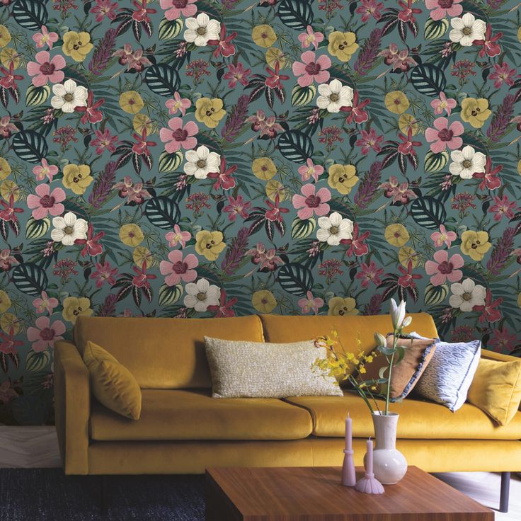 a yellow couch sitting in front of a wall covered in floral wallpaper next to a wooden coffee table