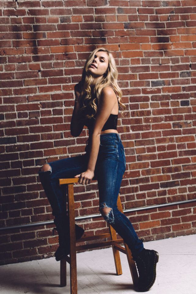 a woman sitting on top of a wooden chair next to a brick wall