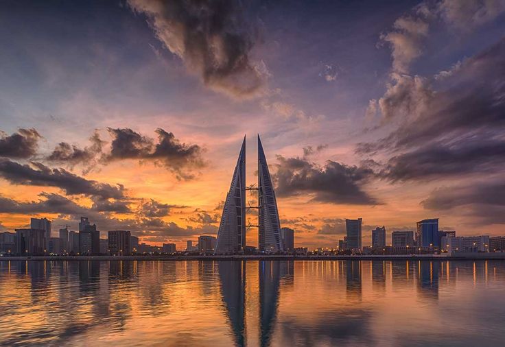 the sun is setting over a large body of water with tall buildings in the background