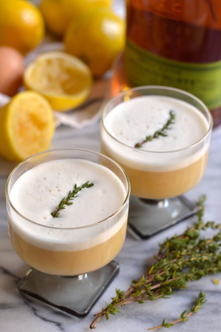 two glasses filled with drinks sitting on top of a table next to sliced lemons