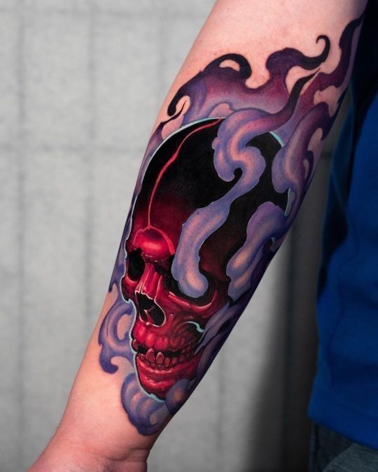 a man's arm with a skull and flames tattoo design on the left forearm