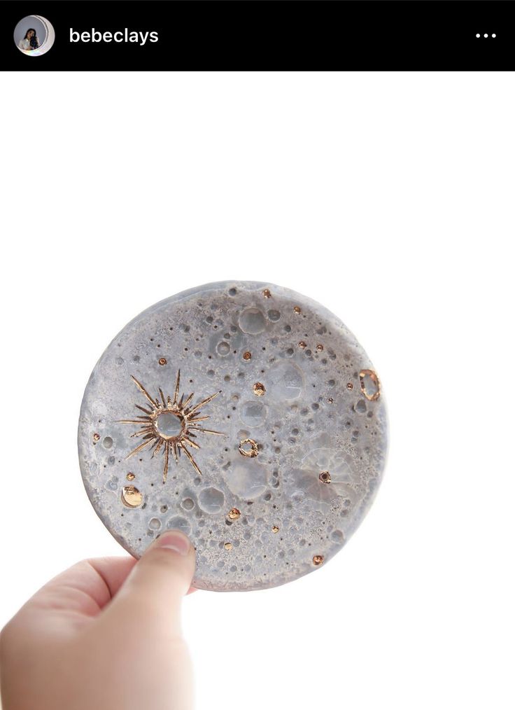 a hand holding a small round object in front of a white background with water droplets on it