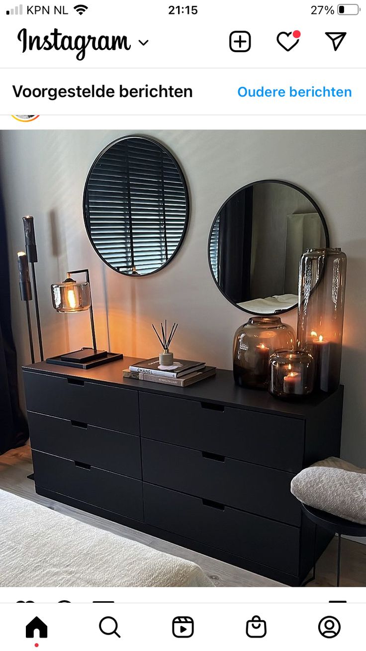 a black dresser with two round mirrors above it and candles in front of the mirror