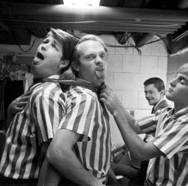 three men in striped shirts are brushing their teeth while another man looks on with his tongue out