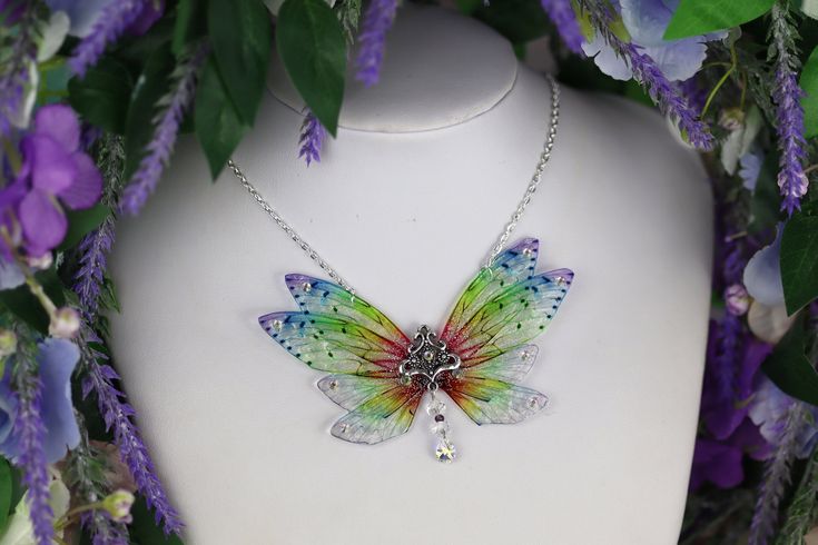 a colorful butterfly necklace on a white mannequin surrounded by purple and green flowers