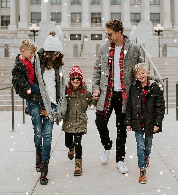 a group of people walking down a sidewalk in the snow with two children and one adult