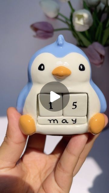 a small penguin clock sitting on top of someone's hand