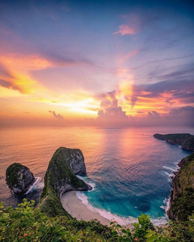 the sun is setting over an ocean with two large rocks in the foreground and another rock outcropping on the other side