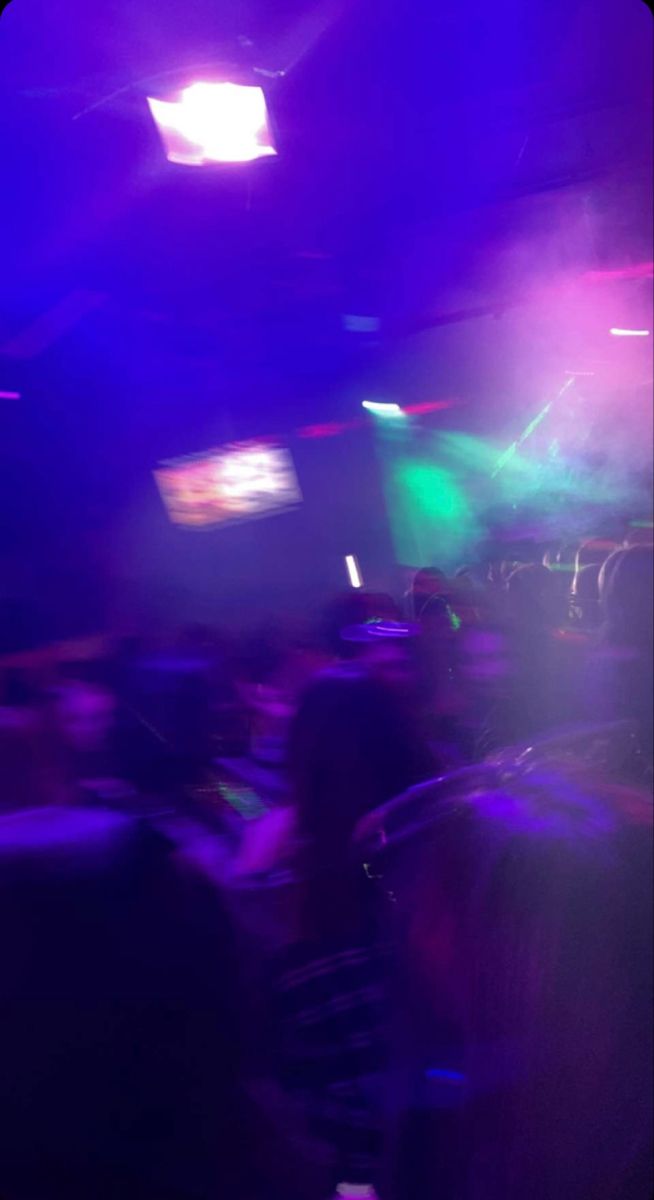 blurry image of people in a club with purple and green lights on the ceiling