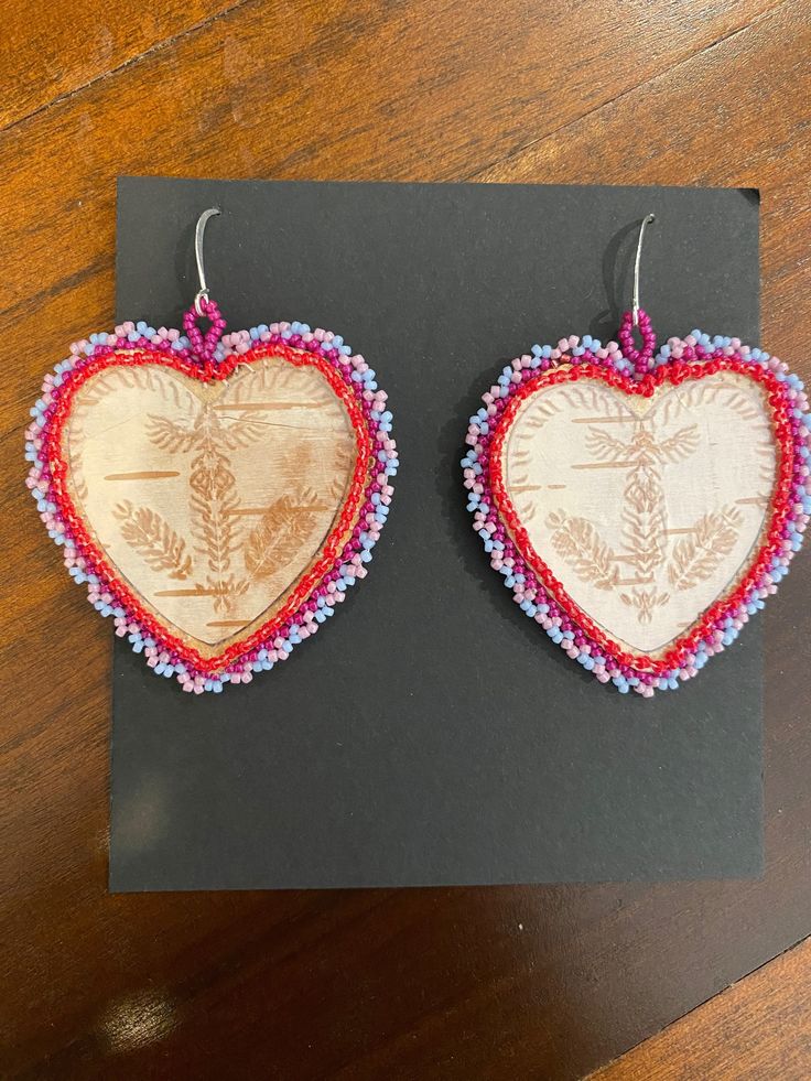 These beautiful earrings are made using birchbark harvested in Wisconsin and finished with beads around the perimeter. The symmetrical pattern on the birch bark is achieved through biting directly onto the bark. The bark is then laminated to protect it. The backing is made out of brain-tanned leather. Bitten birch bark is an ancient native art form. The elder women of the Woodland Nations created this traditional art by biting the birch with their teeth socializing around the campfire. The designs were often used for bead or quillwork.  I am a passionate artist who uses the elements around me to create beautiful pieces of jewelry and art. Everything I make is one-of-a-kind made personally by me in my rural Wisconsin home. Please message with any questions. Thank you for shopping! Birch Bark Earrings, Indigenous Crafts, Birch Jewelry, Symmetrical Pattern, Around The Campfire, Birch Bark, Native Art, Traditional Art, Beautiful Earrings