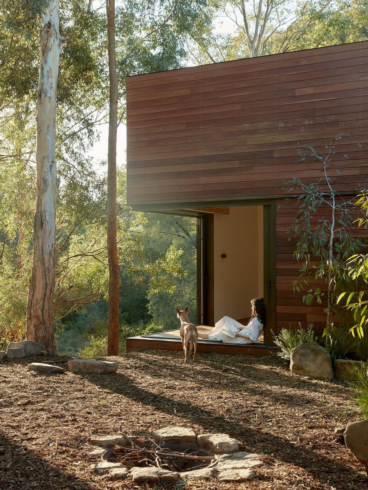 a person sitting on a bench in front of a house with a dog looking out the window