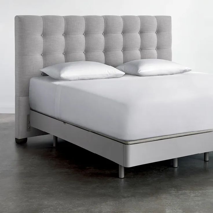 a bed with white sheets and pillows on top of it in a gray floored room