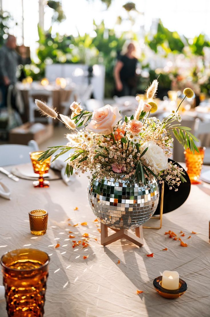 a disco ball centerpiece on a table with flowers and candles in the foreground