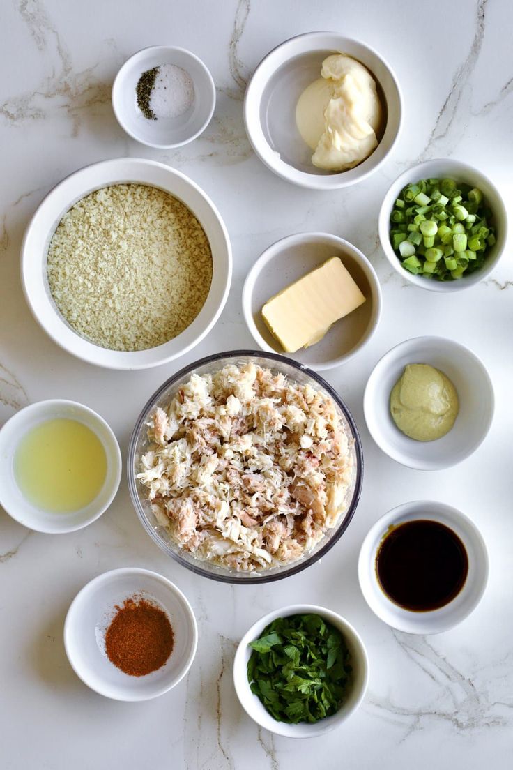 an assortment of ingredients in small bowls on a white counter top, including cheese, sauces and seasonings