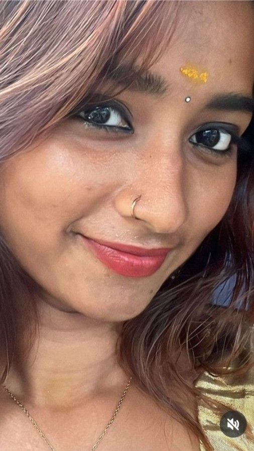 a close up of a person wearing a necklace and piercings on her nose with a smile