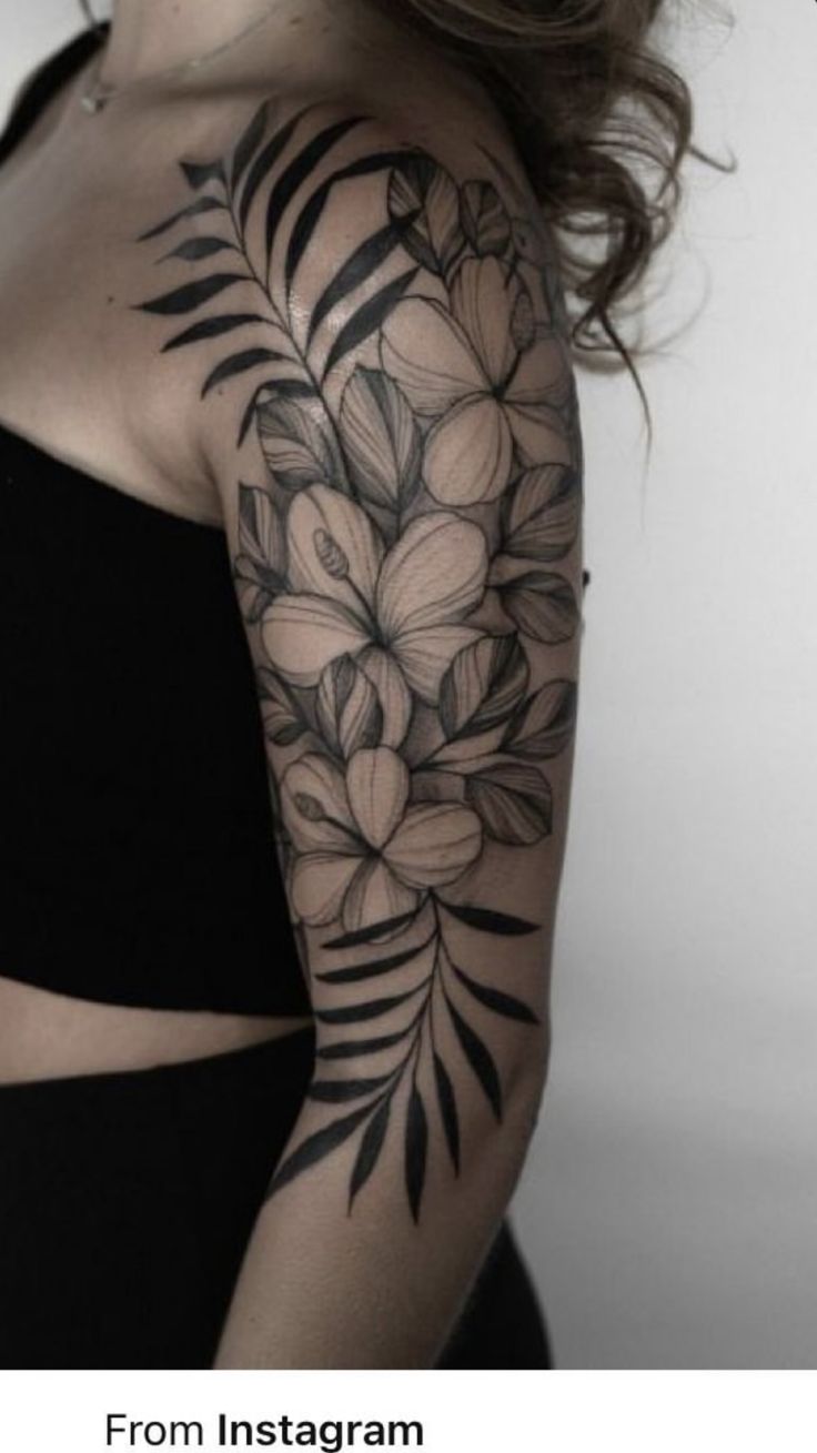 a woman's shoulder with flowers and leaves tattooed on her left arm, in black and white