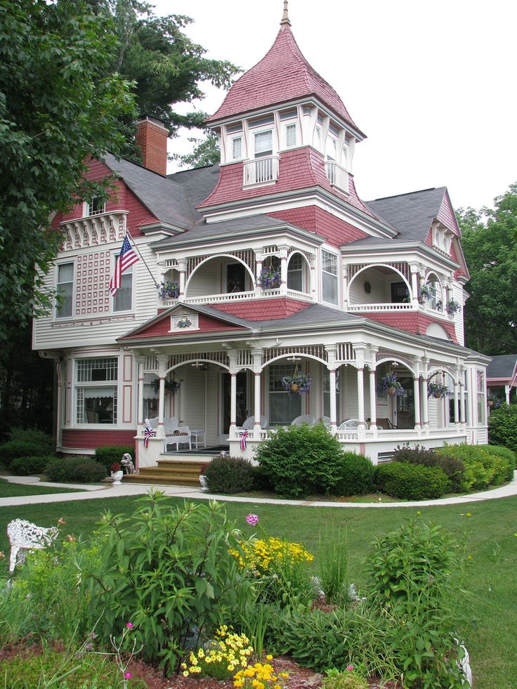 a red and white victorian style house with flowers in the front yard