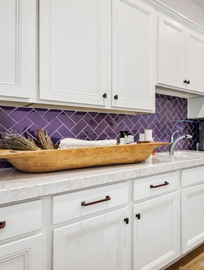 a kitchen with white cabinets and purple backsplash