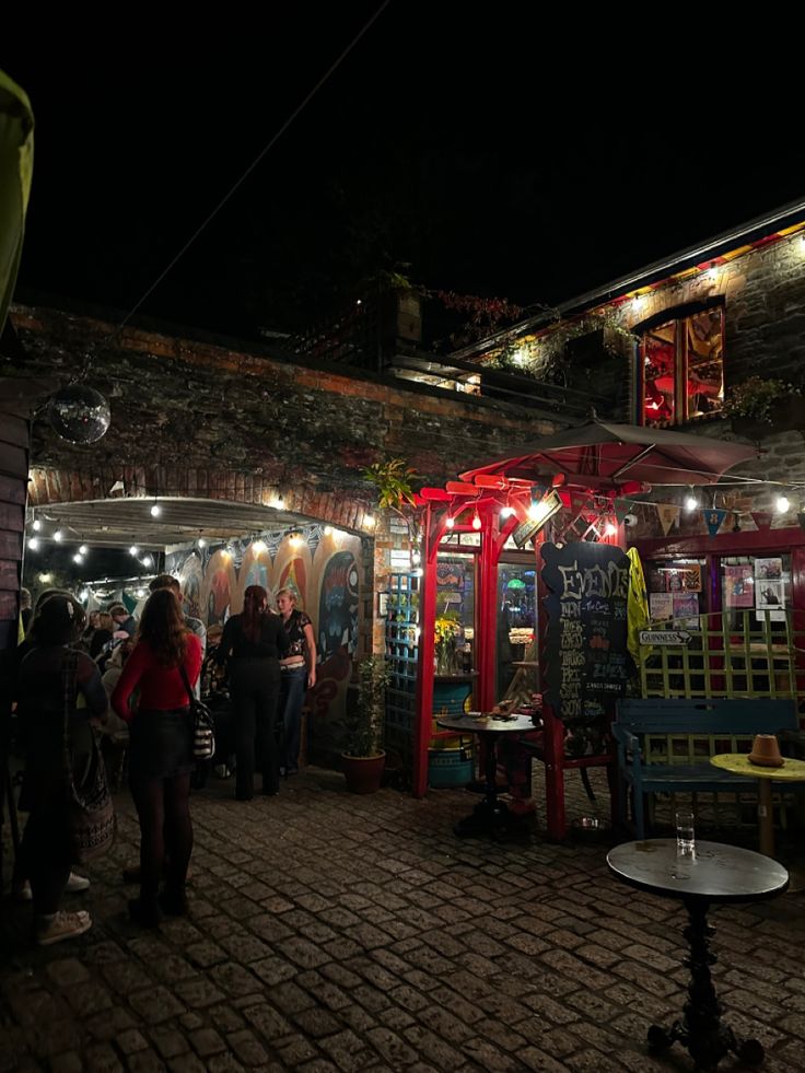 a group of people standing around in front of a building at night with lights on