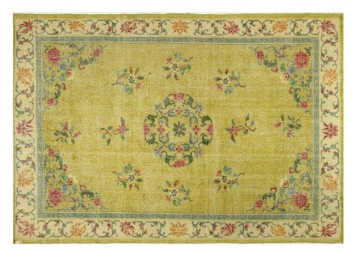 a yellow rug with floral designs on the bottom and green border, in front of a white background