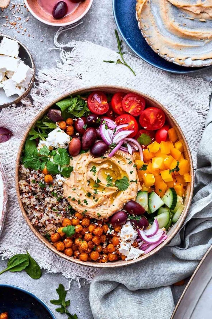 a bowl filled with different types of food on top of a white table cloth next to plates