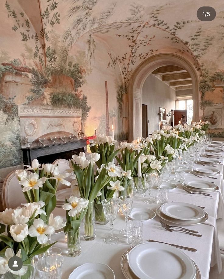 a long table with white plates and flowers in vases